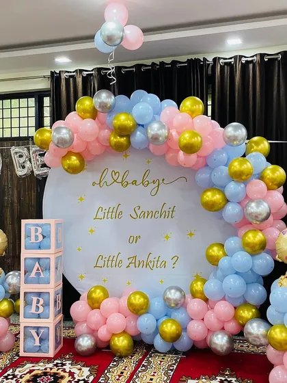 A classic "He or She" gender reveal party setup. This design uses a pink and blue balloon arch with gold and silver accents, 'BABY' blocks, and baby-themed foil balloons to build excitement for the big announcement.
