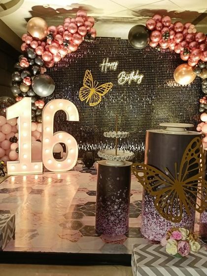 A chic and trendy 'Sweet 16' party with a black shimmer wall, rose gold balloons, and butterfly accents for a modern look.