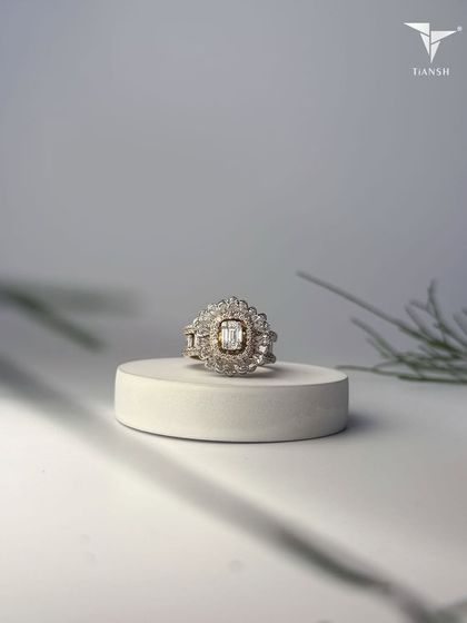 This ring, with its floral halo and radiant baguette-cut center, echoes the delicate poetry of petals cast in gold and light.