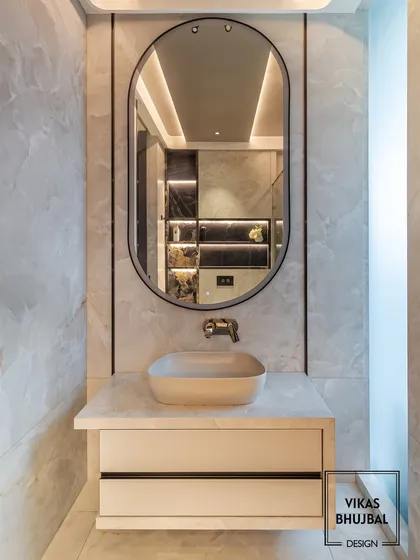 This powder room features a minimalist design with a vessel sink on a floating counter. The oval mirror reflects the clean lines of the space, while the marble wall adds a touch of natural elegance.