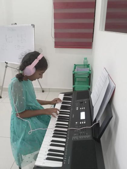 A young student practicing on the keyboard with her headphones on.