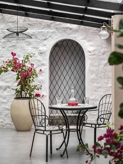 A close-up of the patio seating, featuring a mosaic-tiled table and classic wrought-iron chairs. It’s the perfect spot for a morning coffee or an evening glass of wine, surrounded by blooming bougainvillea.