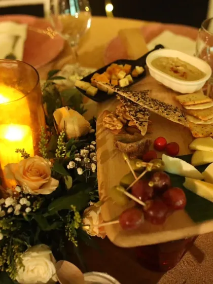 A candlelit table centerpiece featuring a rustic wooden board with an assortment of cheeses, crackers, and fresh grapes. This creates a warm, inviting, and interactive dining experience.