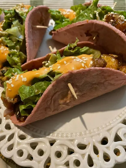 Our Korean-inspired tacos feature crispy chicken tossed in a flavorful sauce, served in a pink beetroot tortilla with fresh lettuce and a drizzle of spicy mayo.