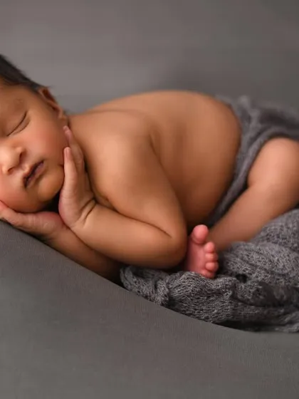 The perfect, peaceful newborn pose. As a certified newborn photographer, I ensure your baby is safe and comfortable to capture these sleepy, curled-up moments. This classic shot on a simple grey backdrop highlights the delicate features of this sweet baby boy.