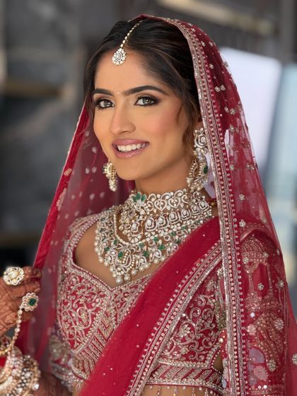 A happy bride on her wedding day. This look features a soft smokey eye and a neutral lip to complement her intricate red lehenga, a versatile style you'll learn.