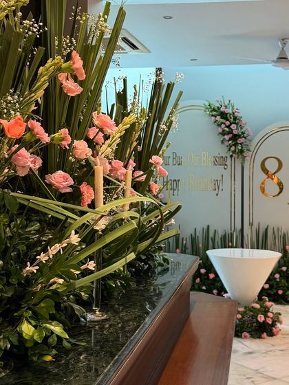 A wider view of the 80th birthday setup, showing how the floral arrangements on the bar tie in with the stunning backdrop. The entire room was filled with pink roses and greenery, creating a cohesive and beautiful design.