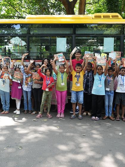 A happy group of children wave in front of the 'Sound Space on Wheels' bus. After a session of musical storytelling and receiving new books, their smiles say it all.