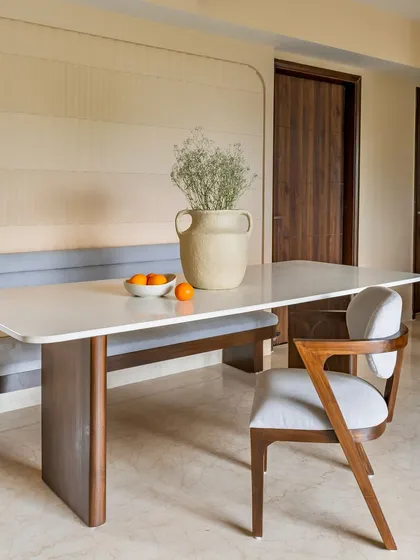 A modern dining space from 'Project Lily' with a sleek white table, a comfortable upholstered bench, and a stylish wooden chair against a textured wall.