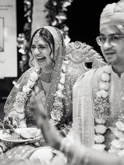 A candid black and white shot of the bride's infectious laughter during a wedding ritual, showing the joy and spontaneity of the day.