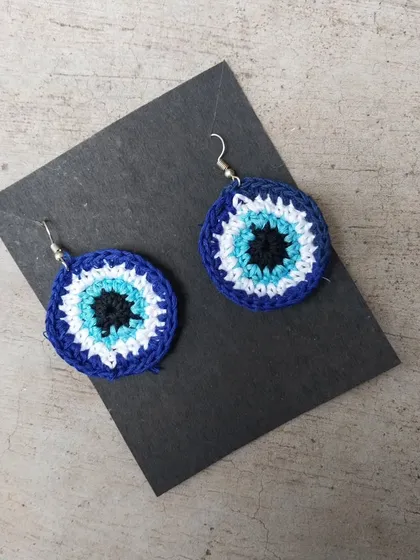 A close-up of the crochet evil eye earrings, showing the detailed color work.