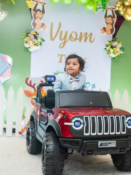 The birthday boy having a blast in a red toy jeep, a fun action shot from his first birthday party.