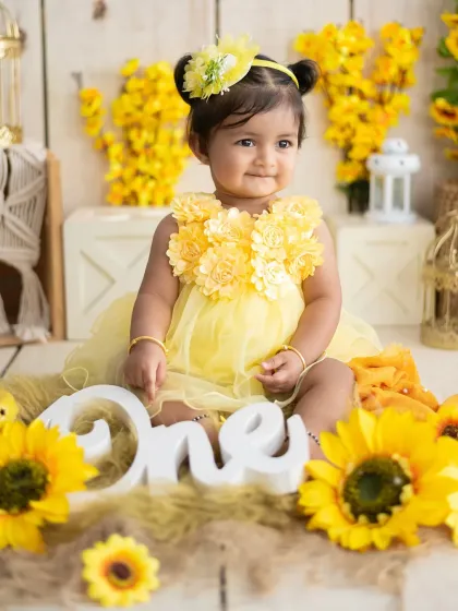 This smiling girl is the star of her sunflower-themed shoot. The setup includes a "One" sign to mark the special milestone.
