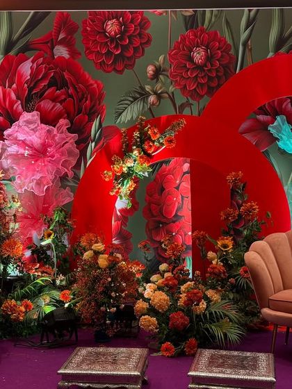 A full view of the eclectic and vibrant stage decor. The design fearlessly mixes colors, patterns, and textures, including a floral wallpaper, red arches, and multi-colored floral arrangements, for a truly unique and celebratory look.
