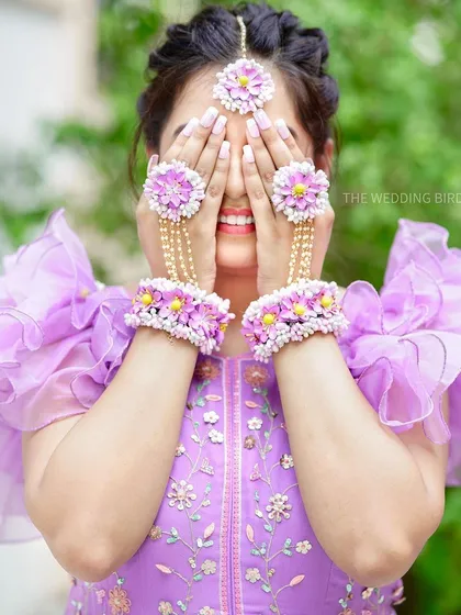 A playful mehendi portrait. The bride hides her smiling face behind her hands, showing off her beautiful floral jewelry and the joy of the occasion.