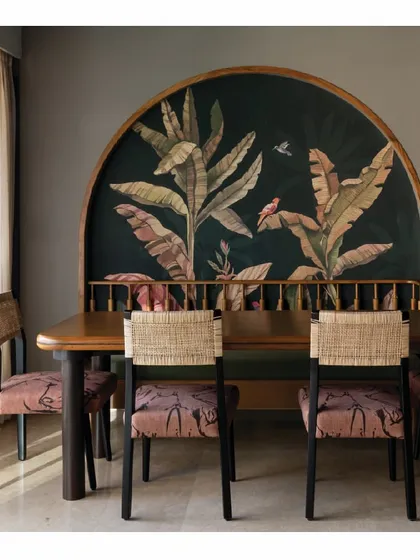 A conversational dining space from our Powai House project. A large, arched tropical mural serves as a dramatic backdrop for the dining table. The chairs, with their woven backs and patterned upholstery, add texture and character, creating an inviting space for meals.