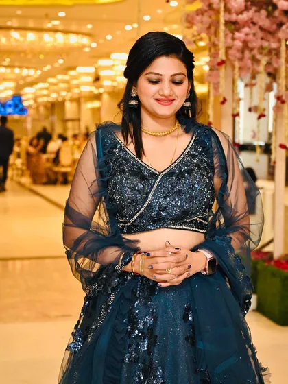 An elegant party look for a client in a deep blue lehenga. Her makeup is soft and glowing, and her hair is styled in a simple half-updo, perfect for a sophisticated evening event.