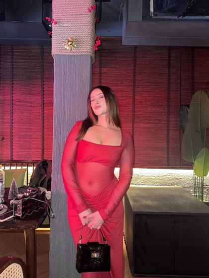 Another pose in the sheer red dress, holding a black clutch.