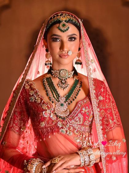 A close-up portrait focusing on the bride's face, framed by the beautiful mathapatti, nath, and layered necklaces. The lighting highlights the sparkle of the stones.