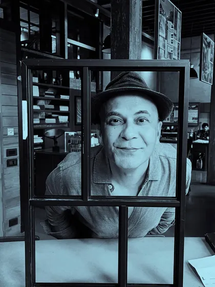 A portrait of Puran Kumar looking through a window frame, a playful moment captured in the studio.