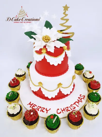 An elegant two-tier red and white Christmas cake, decorated with a large sugar poinsettia and surrounded by matching cupcakes.