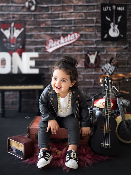This little rockstar is ready for his first world tour! The leather jacket, gold chain, and guitar create a super cool vibe for a first birthday photoshoot.