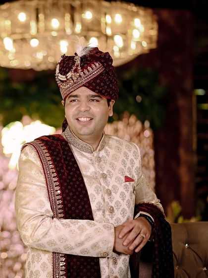 A happy portrait of the groom in his elegant sherwani and velvet turban. The grand chandelier in the background adds to the festive and royal feel of the wedding.