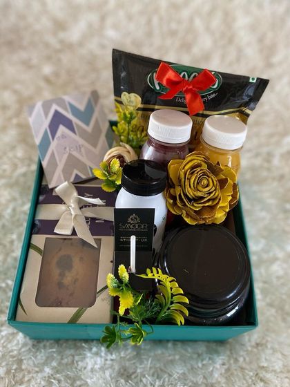 This care hamper is packed with a variety of healthy and comforting items. It includes juices, a plum cake, and other snacks, all arranged in a neat gift box to send some positive energy.