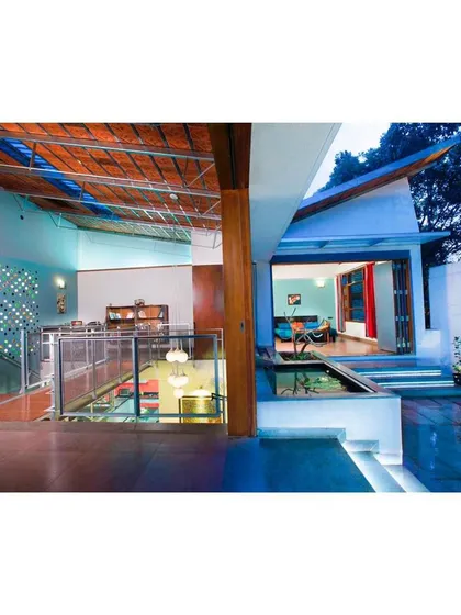 The Interlocking House extension features sliding folding partitions that dissolve the boundary between inside and out. The bedroom transforms from an intimate, enclosed space into a large, semi-open tropical veranda. A butterfly roof with a central spout channels rainwater into a lily pond, connecting the home to the cycles of nature.