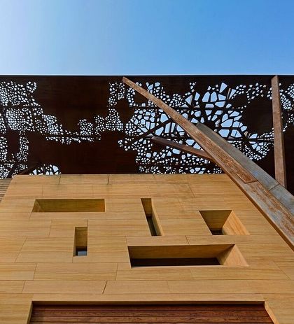 A low-angle view of the Tree House, emphasizing the tree-like columns that support the perforated roof. The geometric cutouts in the stone facade below add another layer of detail and control the light entering the home.