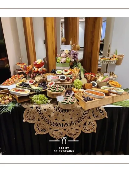 An elegant grazing table with a rustic touch, featuring a beautiful jute table runner. The setup combines wooden platters and tiered stands to display a variety of appetizers, cheeses, and fruits.
