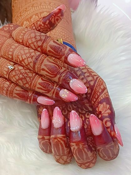 A beautiful example of how ombré nails can be perfect for a bride. This set features a soft pink-to-white fade, with one nail showcasing a delicate 3D flower, all designed to look stunning with her mehndi.