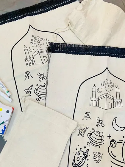 A closer look at the "Colour, Create, Pray" prayer mat for kids. The design features the Kaaba, planets, and stars, ready to be colored in with the included fabric markers, making prayer time a creative and engaging experience.