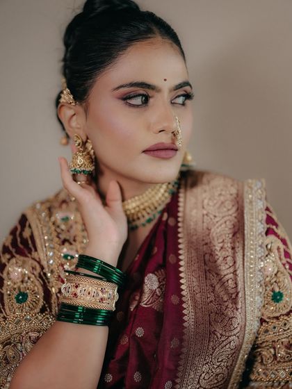 A close-up of the side profile, showing the seamless blend of the makeup and the intricate details of her jewelry, including the classic nath and green glass bangles.