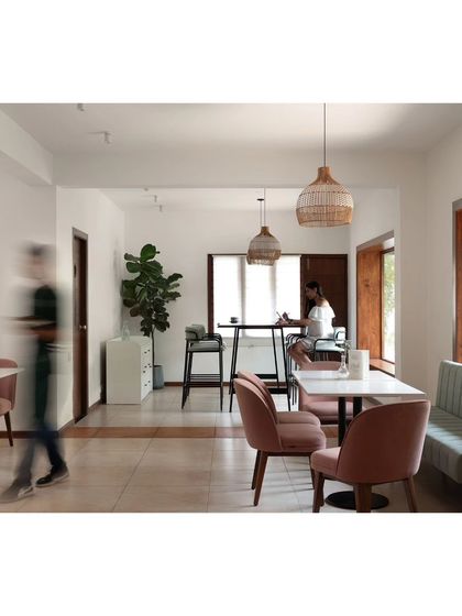 A view of the upper floor's community table, featuring a long wooden live-edge surface. This area is designed for small informal meetings or gatherings, overlooking the lush green surroundings through a large window.