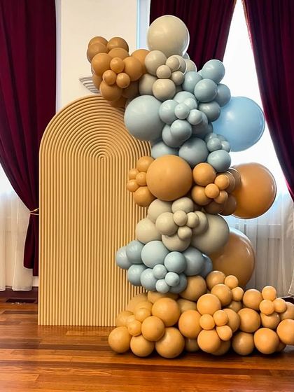 A modern and artistic balloon sculpture in shades of blue, brown, and beige, set against a textured arched backdrop, perfect for a stylish baby shower.