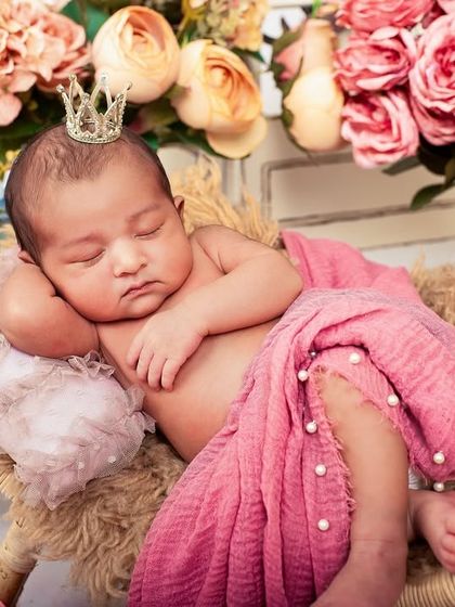 A little princess in her floral kingdom. This newborn is adorned with a tiny crown, nestled among a bed of beautiful flowers.