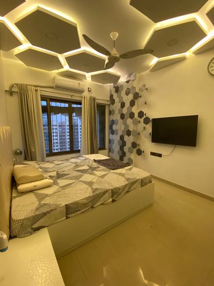 A master bedroom designed with a unique hexagonal theme. The geometric pattern on the TV wall is complemented by a stunning false ceiling with backlit hexagonal panels.