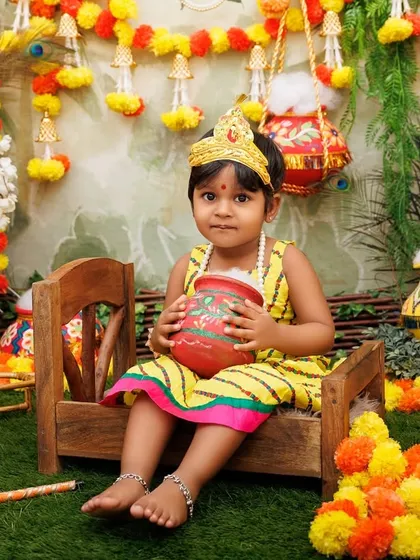 A little girl dressed as Radha sits on a wooden bench, holding a matki, in a classic pose from our Janmashtami sessions.