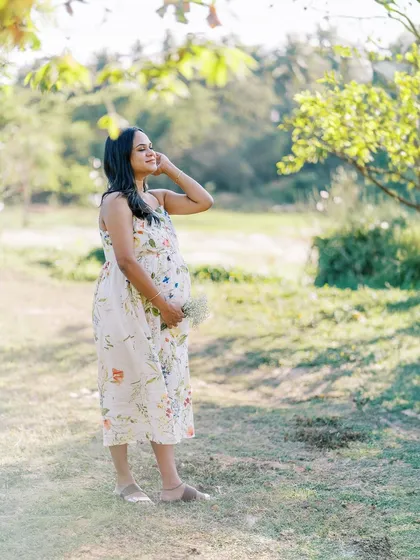 A wide shot of the mother-to-be standing in a beautiful, sunlit clearing. This image shows the scale of the natural landscape and her peaceful presence within it.