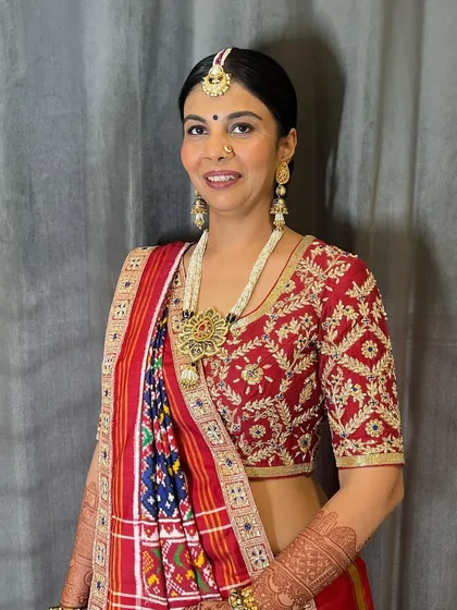 The front view of the client with her classic braided bun, showing how the sleek front complements the traditional updo. The maang tikka sits perfectly with this style.
