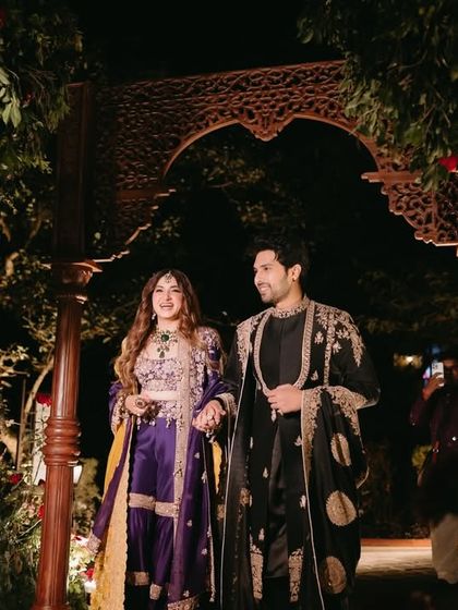 The couple makes a grand entrance through a custom-built wooden arch adorned with florals and lights for their "Perfumed Orchard" Mehfil-e-Mehendi.