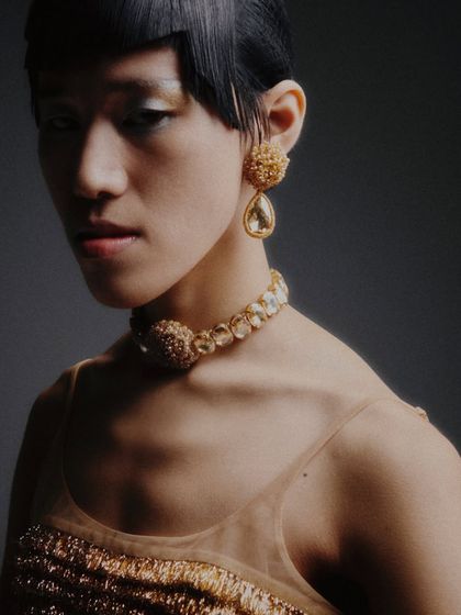 A beautiful close-up on the jewelry set, including a statement choker and drop earrings. The model's pose and expression are soft and elegant.