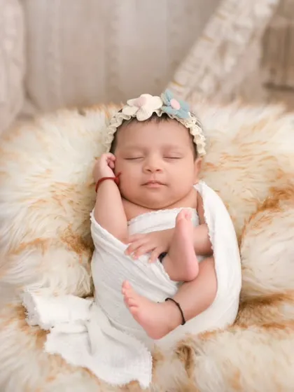 A peaceful newborn rests on a soft, cream-colored fur, adorned with a delicate floral headband. This photograph highlights our skill in posed newborn artistry, creating serene, beautiful portraits that focus on your baby's innocent features against a gentle, boho-inspired backdrop.