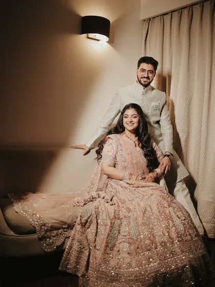 A classic portrait with a touch of affection. The groom stands behind his seated bride, his hand gently on her shoulder, creating a sense of love and support.
