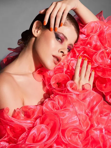 A high-fashion look where the makeup is paired with a dramatic, ruffled outfit and bright orange nails.