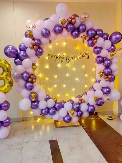 A purple and lilac balloon ring decoration for a 13th birthday. The setup is accented with gold star balloons and a large number '13' foil balloon, set against a backdrop of fairy lights.