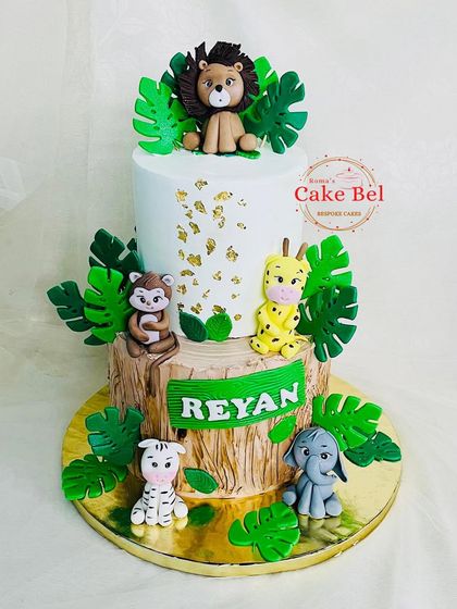 A two-tier jungle cake with a wood-textured bottom tier and a clean white top tier with gold leaf accents. The handcrafted fondant animals add a playful touch.