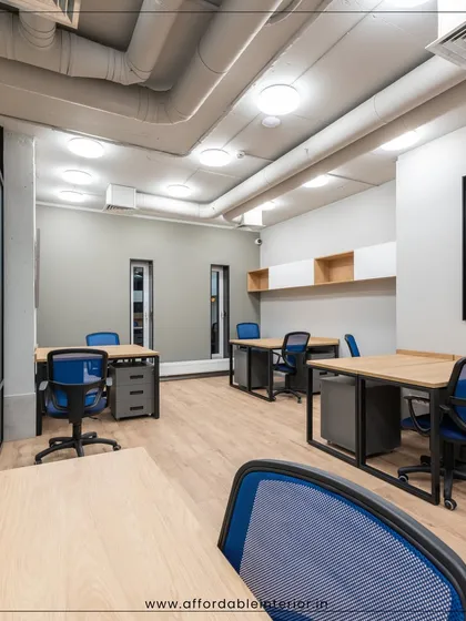 This co-working space is designed for flexibility and collaboration. The layout features individual desks with ergonomic blue chairs and an industrial aesthetic with exposed ceiling pipes, catering to a modern workforce.