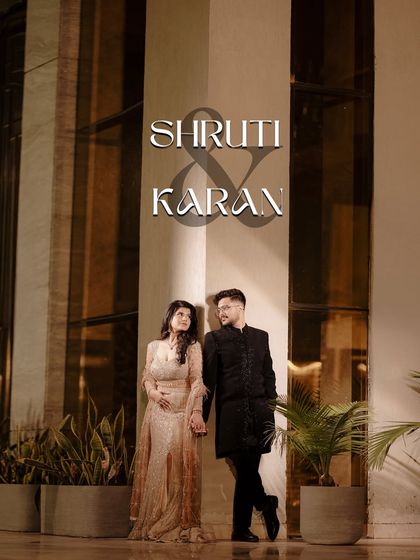 A stylish full-length portrait of a couple against a modern, warmly lit wall. This shot is perfect for showcasing their coordinated outfits and confident elegance in a contemporary setting.